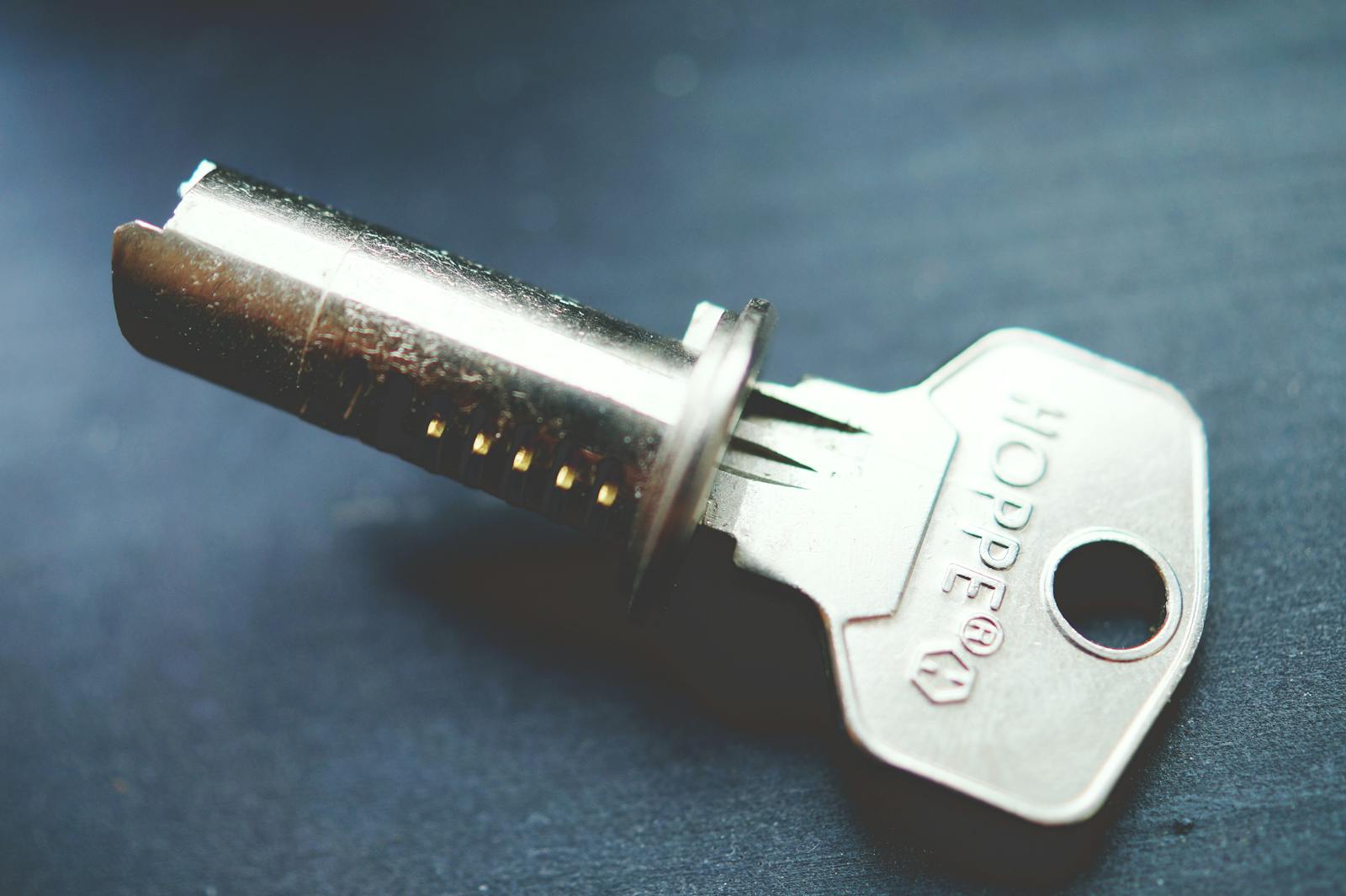 Detailed close-up image of a metallic key with lock cylinder on a dark surface, highlighting intricate details.